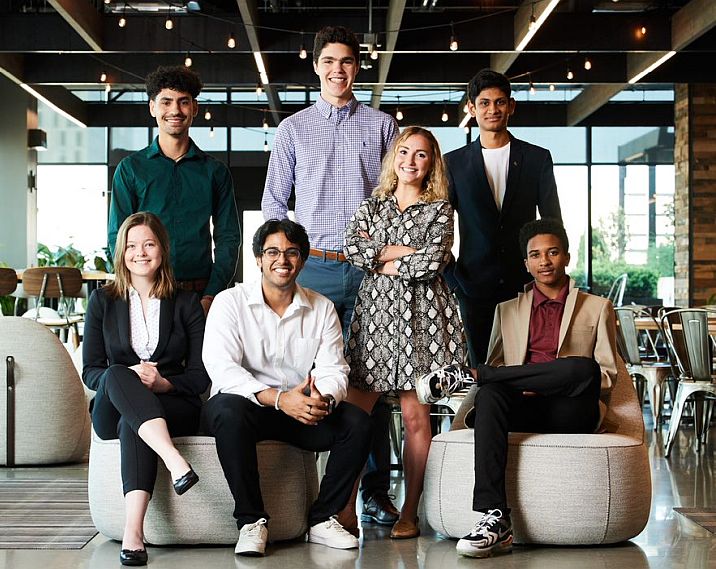 A group of college students in business casual dress pose together smiling.